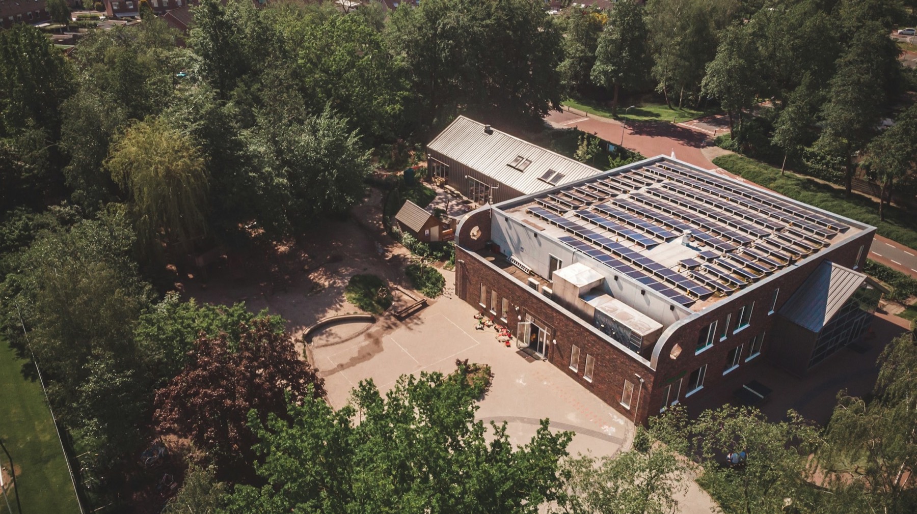 Aerial view of a brick building with solar panels across its roof, surrounded by trees